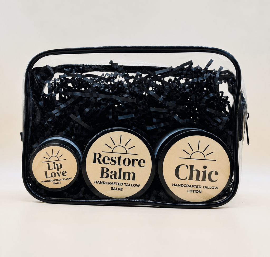 A clear zippered cosmetic pouch filled with black shredded paper and three round tins of handcrafted tallow salves  and lotion labeled Lip Love, Restore Balm, and Chic, on a light beige background.