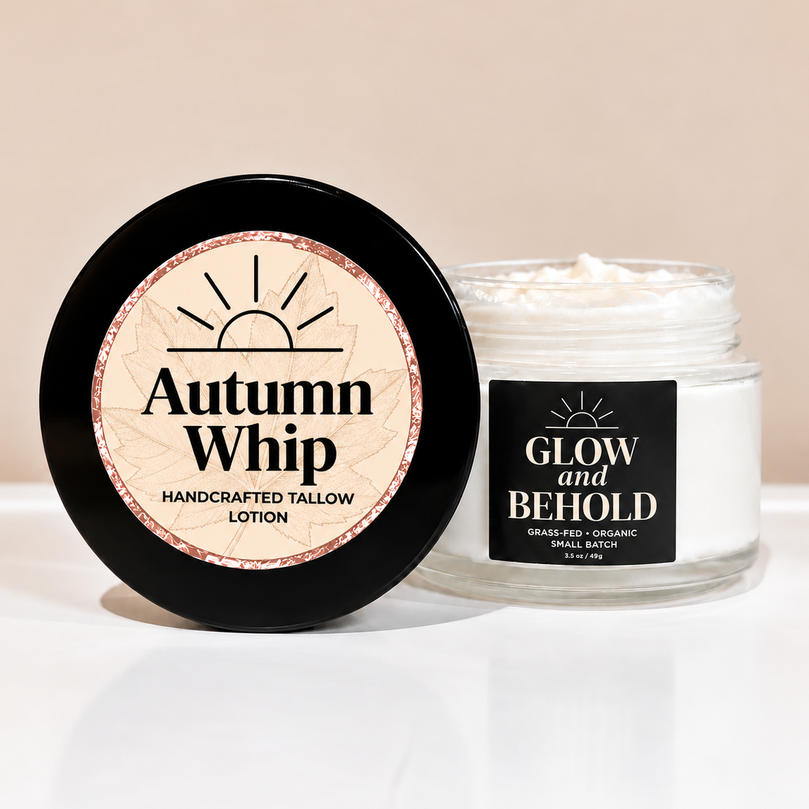 A jar of tallow lotion with its black lid leaning against it on a white surface. The lid label reads 'Autumn Whip Handcrafted Tallow Lotion,' and the jar label reads 'Glow and Behold Grass-Fed Organic Sheep Lactation Grass-Fed Organic Cows Lactation Handcrafted Tallow Lotion.